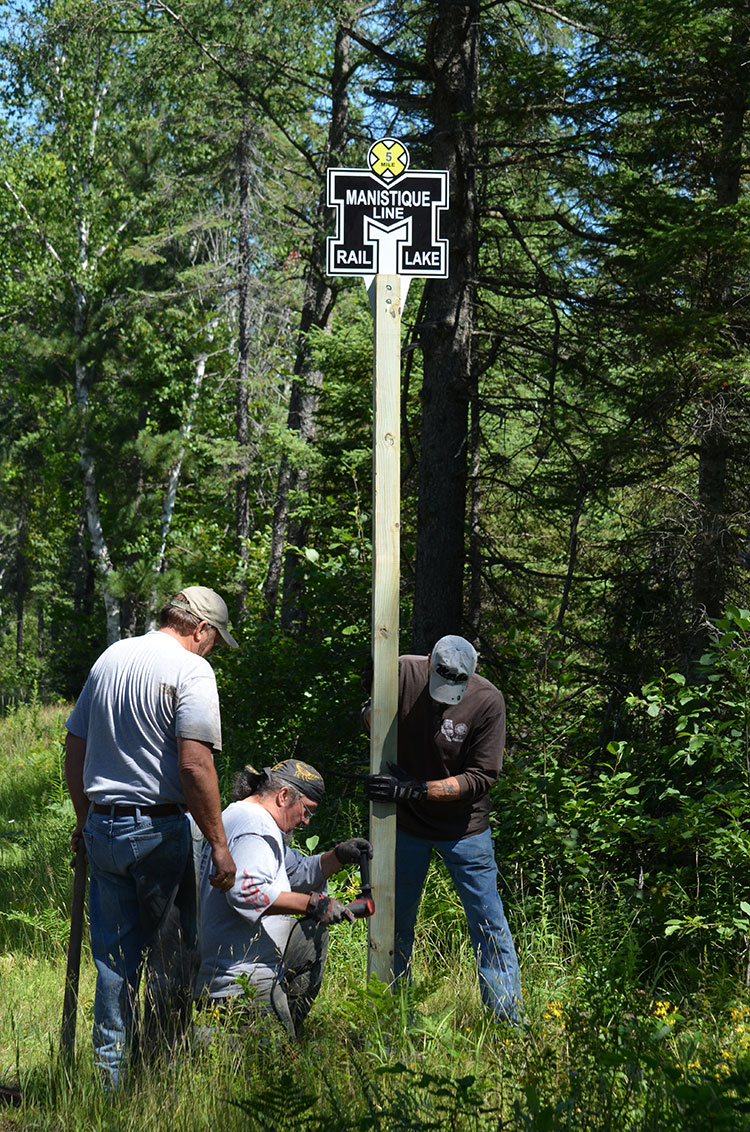 Volunteers installing mile markers with the historic Manistique Line logo (which used to operate on the corridor). On the Haywire Trail in the UP, Michigan’s oldest rail trail. Credit: Dan Spegel