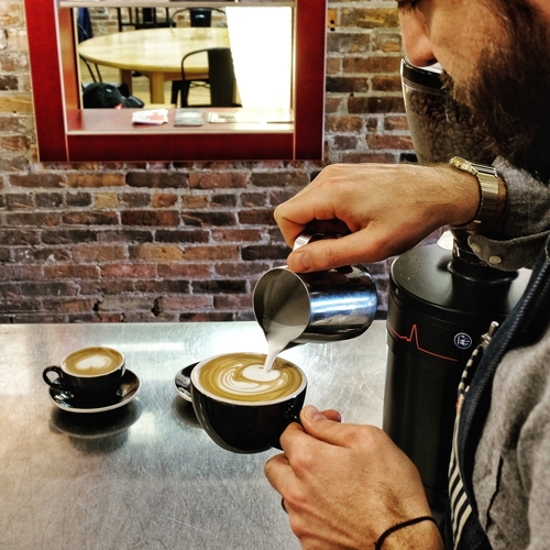A barista pours a latte at Mighty Good Coffee.