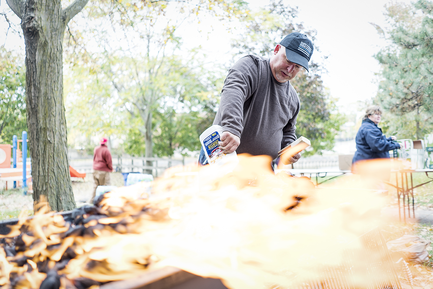 Volunteer and Davison resident Steven Moore, 52, squeezes lighter fluid onto a pile of charcoal briquettes as he prepares the grill for the Flint Community Cookout. 