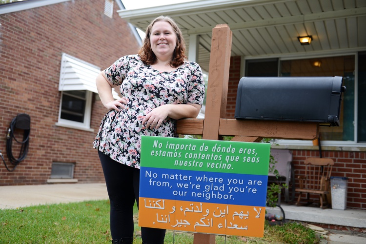 Jessica Woolley, 31, stands in front of her home where the sign welcomes neighbors in three languages. Photo by Jessica Strachan. 