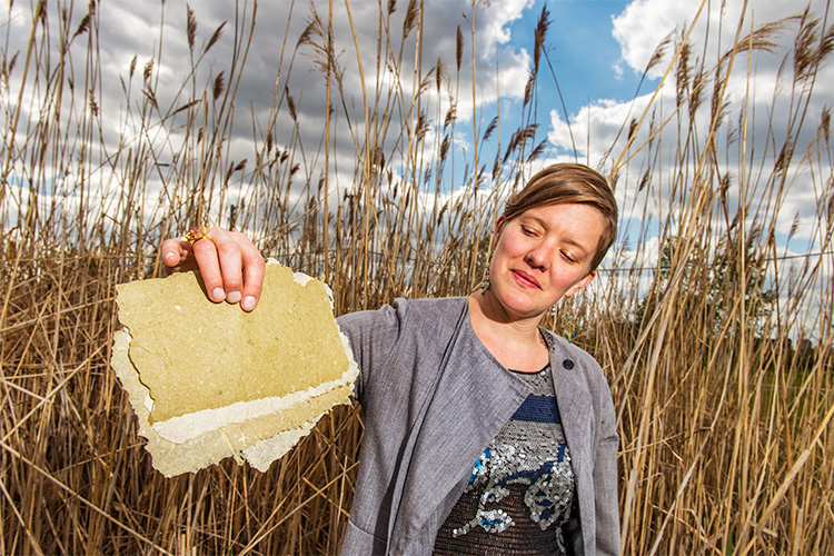 Meg Heeres models phragmites paper near a stand of the invasive plant near Canfield and Grand River.