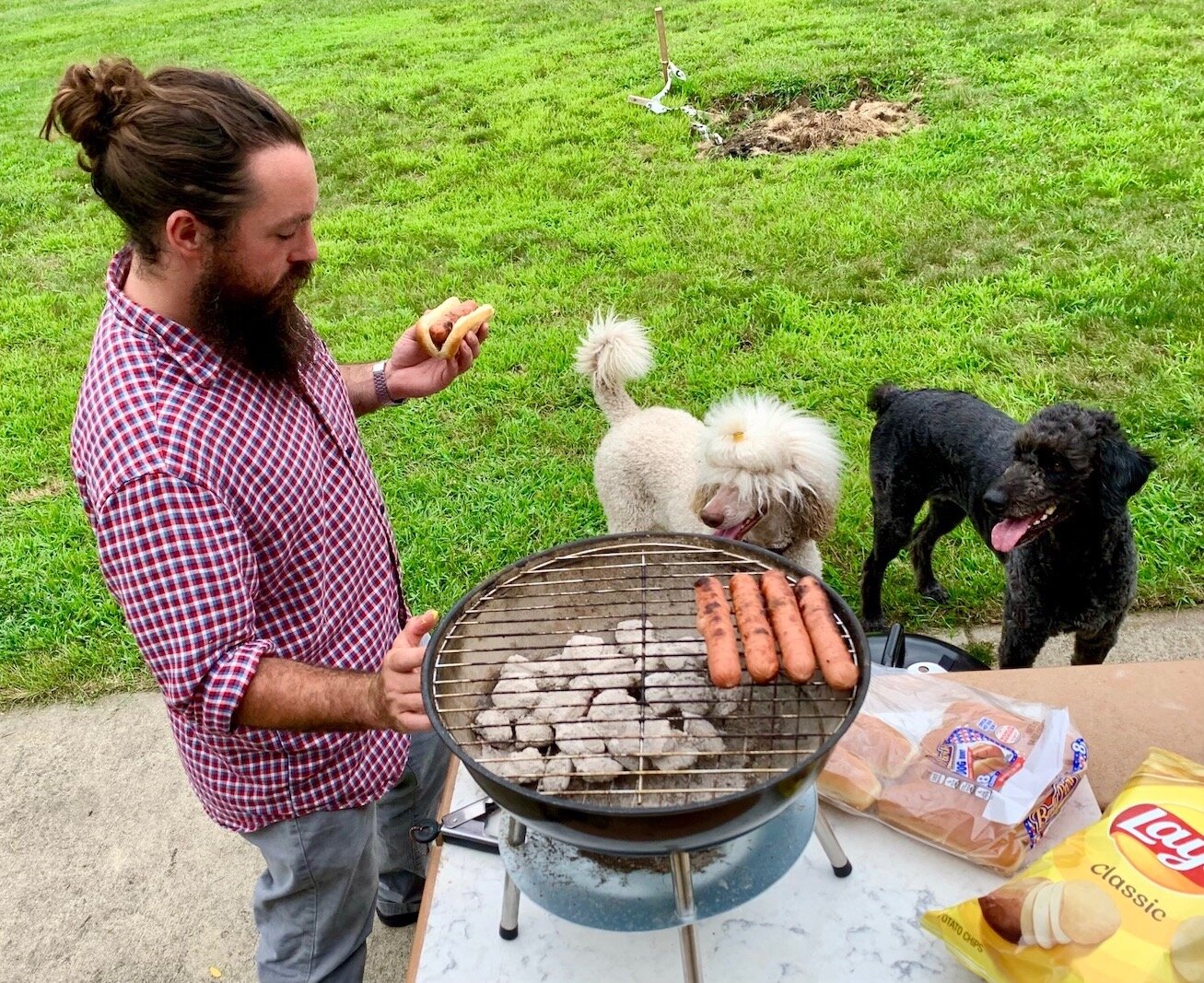 Benjamin Stanley grilled hotdogs on a Thursday afternoon to share with others at Fairmont Dog Park. His white poodle Maisie and black labradoodle Daisey are hoping he drops some food.