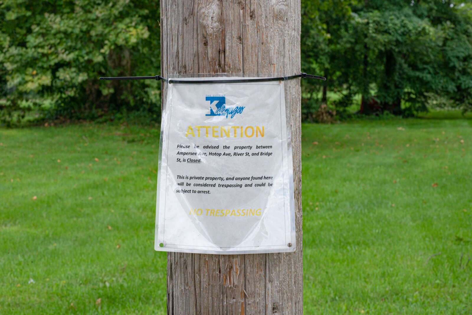 A sign on pole indicates the land is the property of The City of Kalamazoo. It is the site of a previous houseless people encampment from which residents were forcefully required to leave.