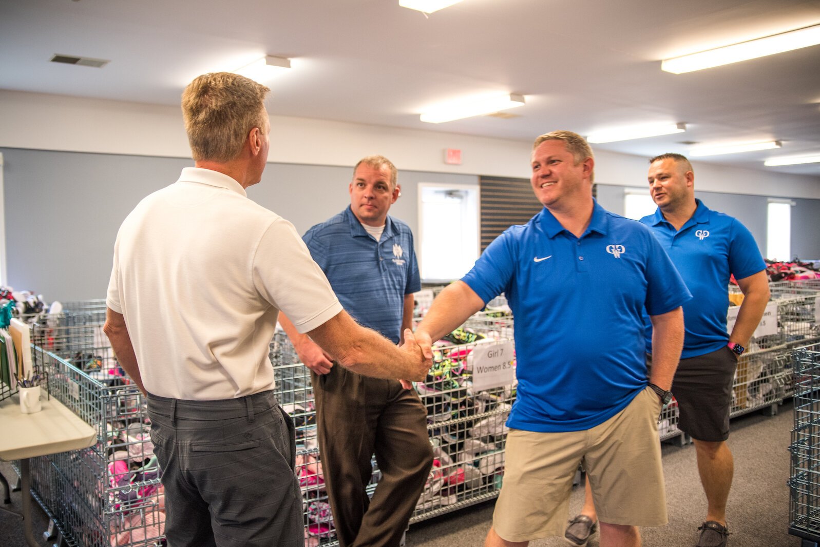 Cody Livingston, president of Guys Who Give – Kalamazoo County, center, shakes hands on Wednesday, June 22, 2022, with group member Scott Everett, in white shirt, after they present a $15,200 donation to First Day Shoe Fund.