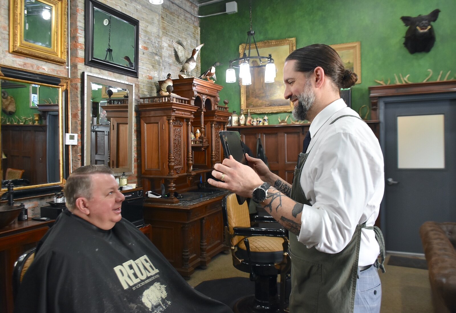 Noah Saber shows customer Richard Morrissette his haircut in the Huntsman’s Hound Lounge in downtown Marshall.