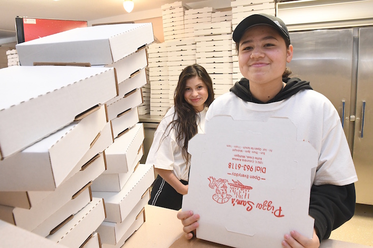 Nicole Wygant, left, photo bombs while her sister Laura folds boxes at Pizza Sam’s.