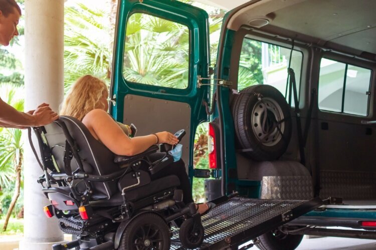La foto muestra a una mujer en silla de ruedas que sube por una rampa a una furgoneta de  transporte accesible. 