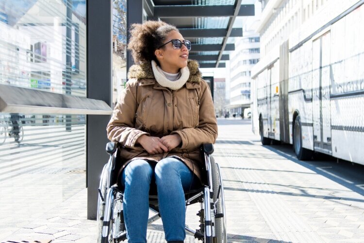Foto de una mujer en silla de ruedas en una parada de autobús.  