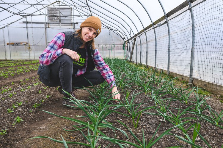 Jae Gerhart, Manager of the Farm at THAA, crouches next to plants growing in a hoop house.