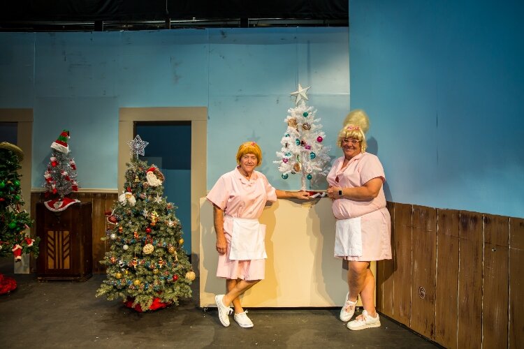 Act Two opens with Miller, at left, and Jacobs portraying two waitresses wearing pink uniforms and working at the Tasty Kreme Restaurant. The restaurant motto is 'Eat Here, Get Gas.'