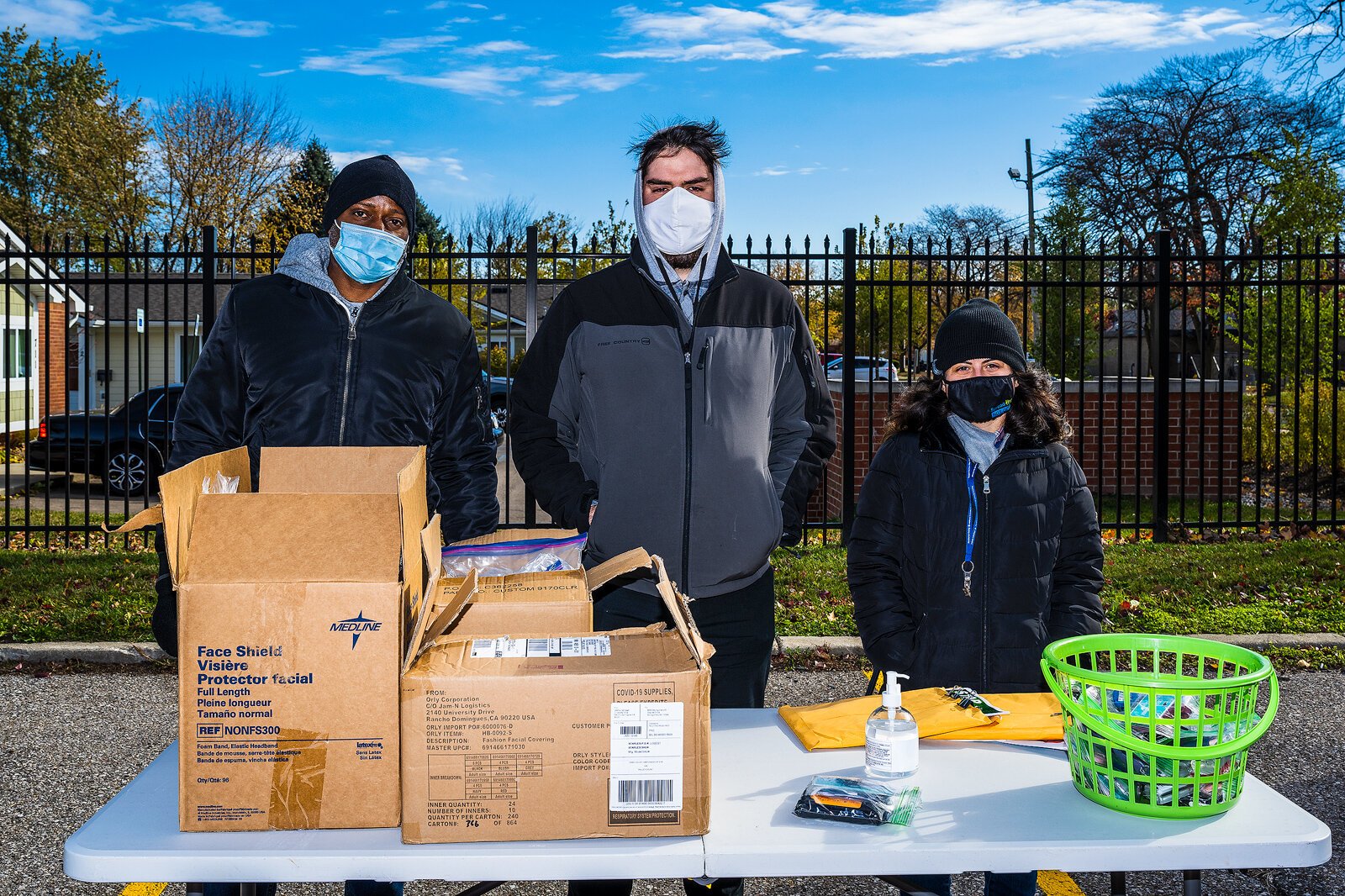 Charles Wilson, Renato Quelhas, and Briana Tetsch hand out free cleaning supplies and masks at a flu shot drive-through/walk-up event in the Washtenaw County Health Department parking lot in Ypsilanti.
