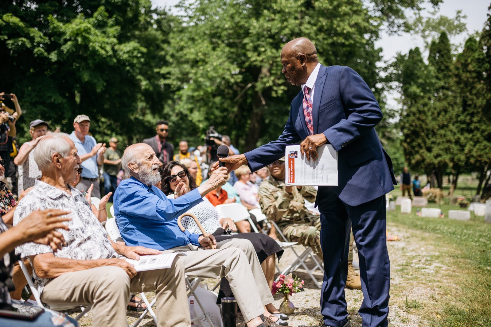 State Rep. Ronnie Peterson hands a microphone to monument sculptor John Pappas.