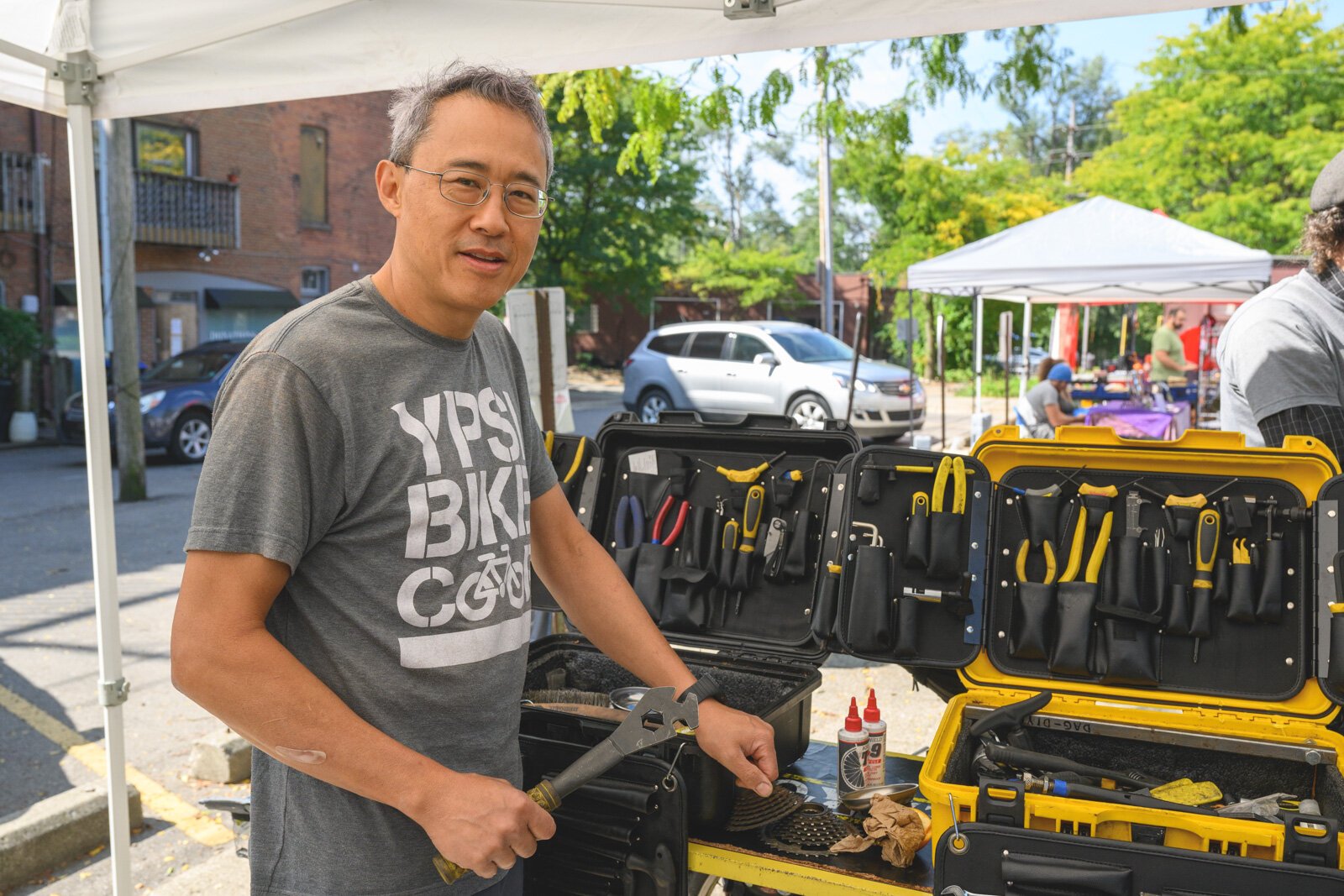 Yitah Wu repairing a bike at the Ypsi Bike Co-op's booth at Ypsilanti's Depot Town farmers market.