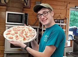 A Mitchell's Gourmet Deli employee shows off a pizza in progress
