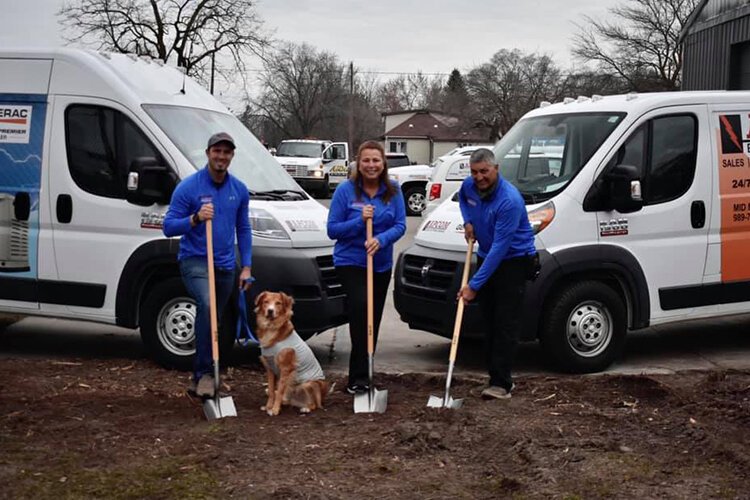 Thomas Howell (left), Vanessa Howell, and William Howell stand with Apcom's mascot Brady posing with shovels indicating the start of the new Apcom.