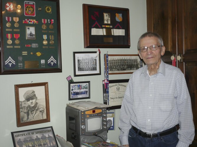 WWII veteran Ed Haynack stands by his wall of memorabilia from his time in the Army.