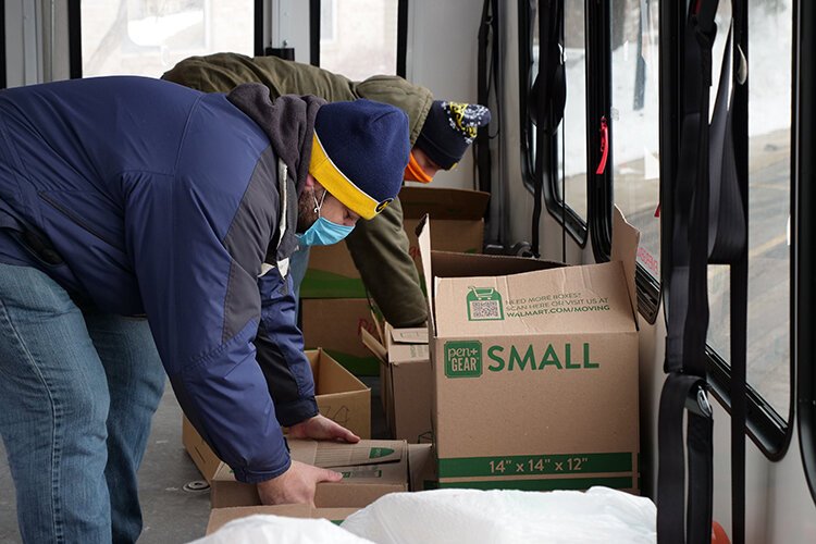 Volunteers Marc Cooper and Caleb Ross pick up boxes from The Care Store that are aboard an I-Ride bus and about to be delivered to local residents.