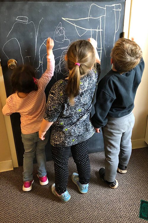 A group of preschool students draw on a chalkboard. 