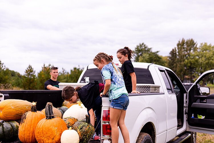 (Left to right) Stella McConnell, 7, Lucy Valentine, 6, and Maeve McConnell, 10, load pumpkins onto a truck bed to transfer produce to the pumpkin display. 