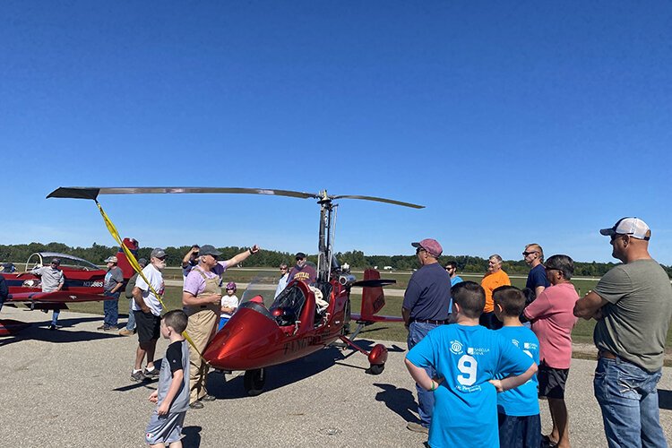 Families and airplane enthusiasts gather around a pilot offering free rides.