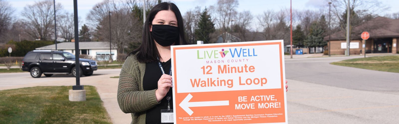 Erin Barrett, a public health planner with District Health Department #10, holds a walking trail sign in Ludington.