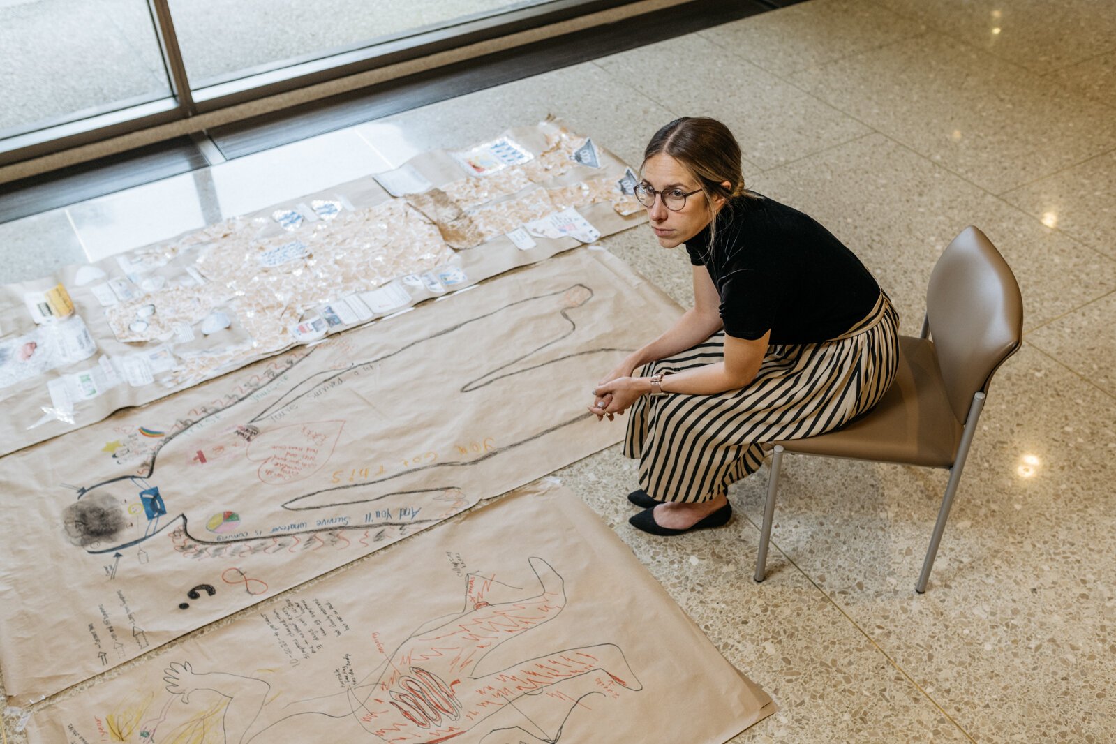 Dr. Sara Santarossa is the lead on a Henry Ford Health project that asked COVID long haulers to draw body maps representing their condition. She sits next to several of their works here.