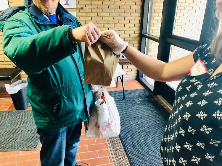 A Community Kitchen worker hands a prepackaged meal to a visitor to the daily kitchen.