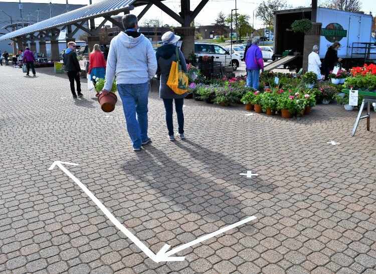 Taped arrows direct the movement of market visitors while an "x" designates safe social distancing.