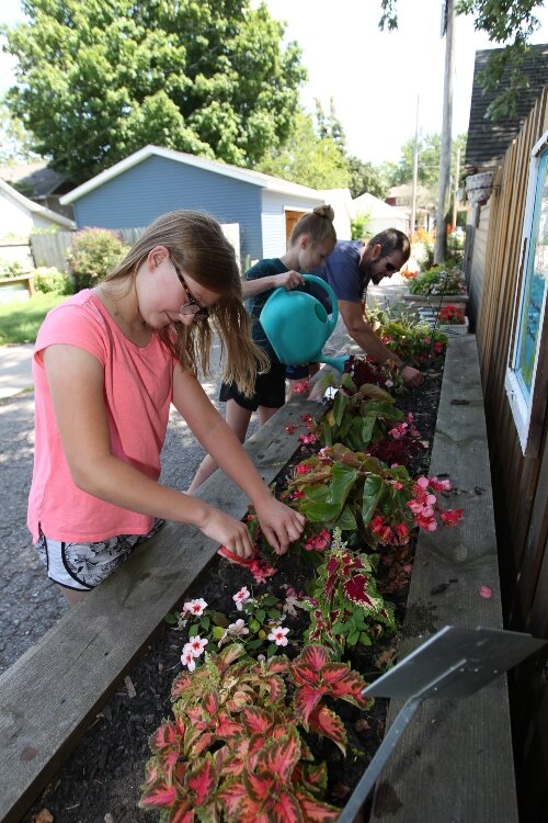 Raelyn Long, 9, trims flowers in a raised bed garden while her neighbors Reese and Jimmy Weeks water and trim the flowers on the opposite end of the garden in the alley between 19th and 18th streets along River and Central avenues in Holland.