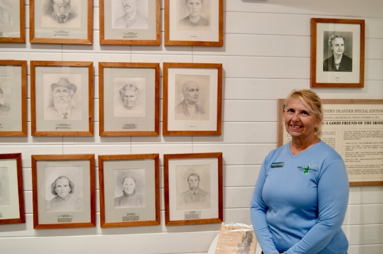 Beaver Island Historical Society assistant museum director Sharolyn Hunter, next to a wall of notable past residents. The lower-right portrait is of Thomas Bedford, one of the assassins of King Strang.