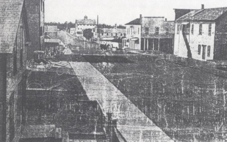 Image of River Street in Holland, Michigan during the Civil War. Buildings line either side of the street, and a carriage is off to one side from the jstor.org/ History of Holland collection.