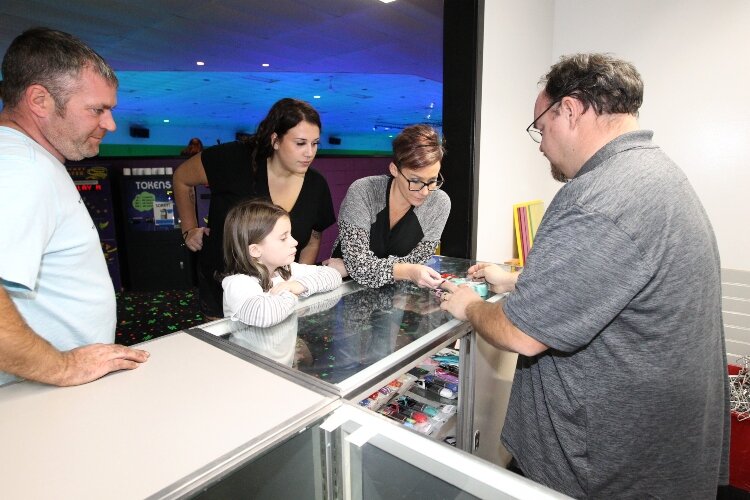 Tim Price, co-owner of RollXscape Skating Center in Holland Township, right, shows skating enthusiast a set of LED quad roller skate wheels in the rink’s skate shop during the venue’s grand opening, Nov. 4.