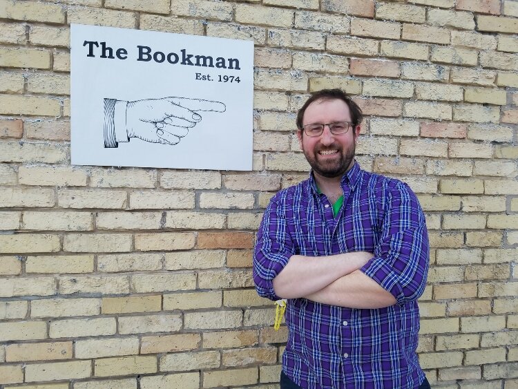 The Bookman in Grand Haven is celebrating the Grand Haven Area Community Foundation's 50th anniversary with a free book giveaway for youth. The Bookman's book buyer Scott Lange poses by the shop's sign.