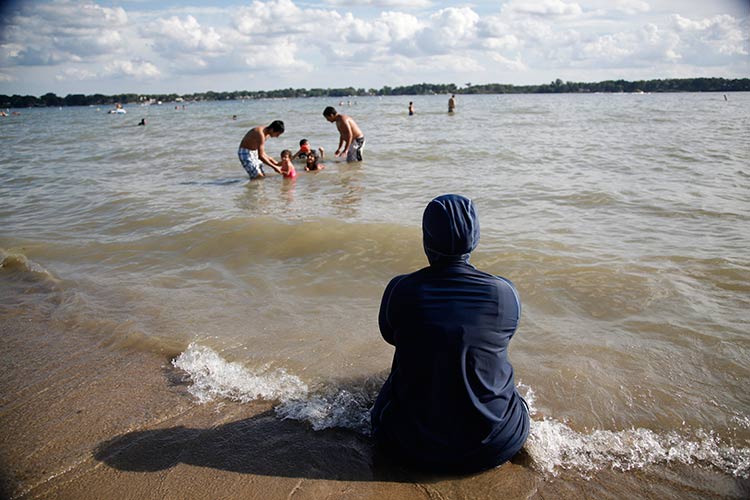 E.H. sits at Cass Lake watching her children swim. Photo by Imad Hassan.