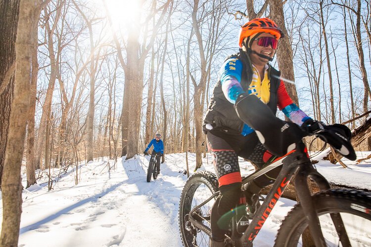 A fat-tire bikers ride with the sun to their backs.