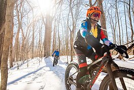 A fat-tire bikers ride with the sun to their backs.
