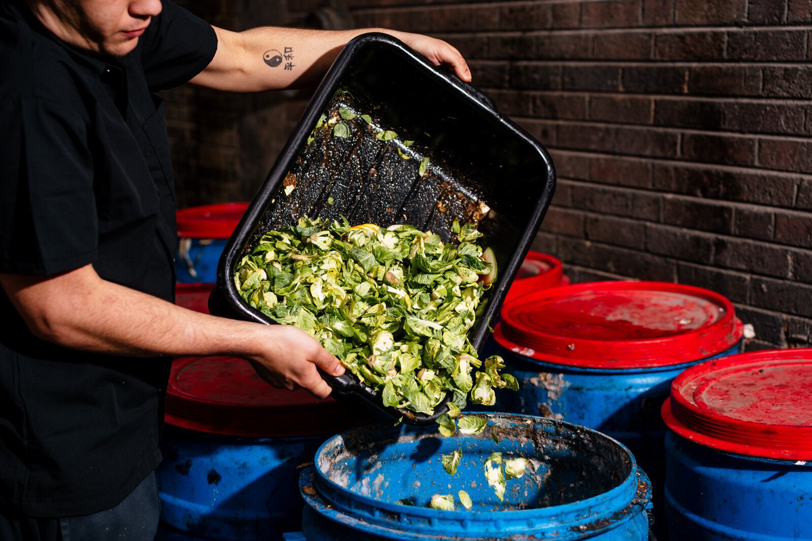 A staff member pours unused brussel sprout leaves into a compost barrel at the Apparatus Room.