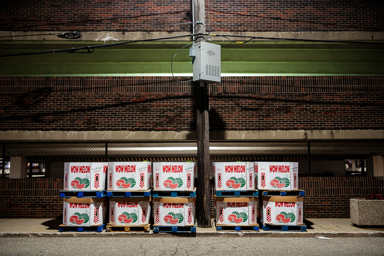 Boxes of watermelons lined up against the parking structure across from Shed 3's parking lot