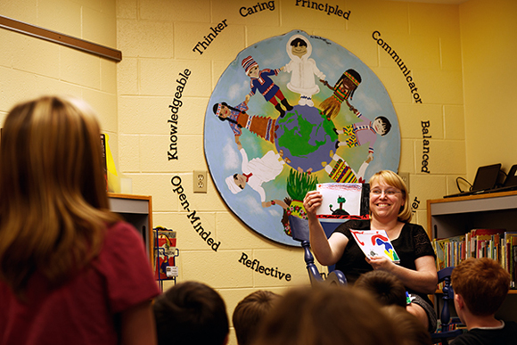 Librarian Beanie Sand discusses sky color drawings with Mill Creek students. The Learner Profile Circle behind her supports students in developing good character.