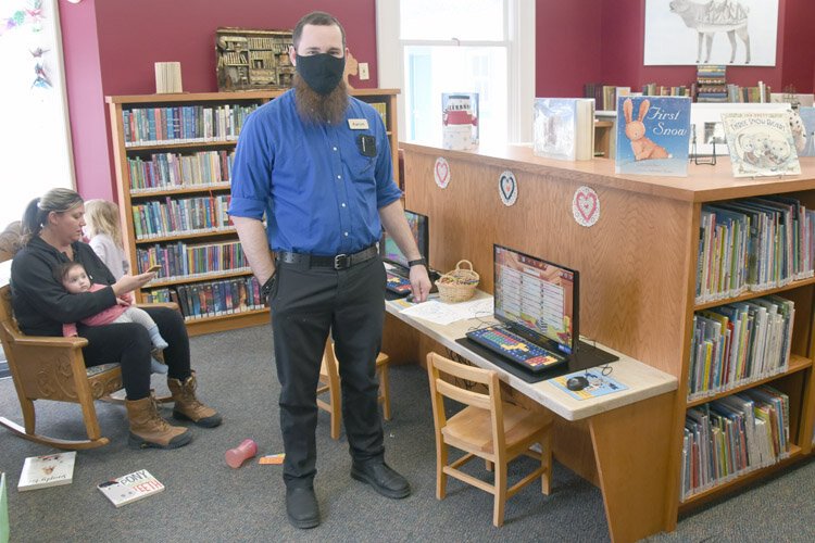 Aaron Hill, IT coordinator for Elks Rapid District Library, stands at computer station in children's reading area.