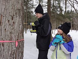 Alex Robbins, 14, and his younger sister Ella, 8, work together to tap a sugar maple tree during a SEEDS EcoSchool family event. 