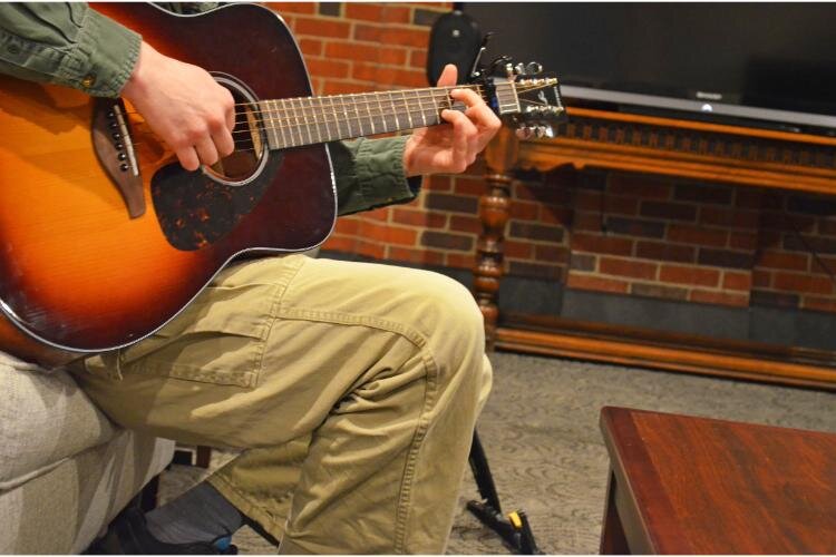 Josh Jerz speaks to the group as facilitator and fiddles on his guitar while the conversation ebbs and flows.