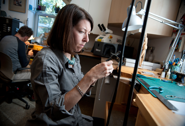 Kara measures out chain for a necklace as Daniel carefully shaves down a custom ring.