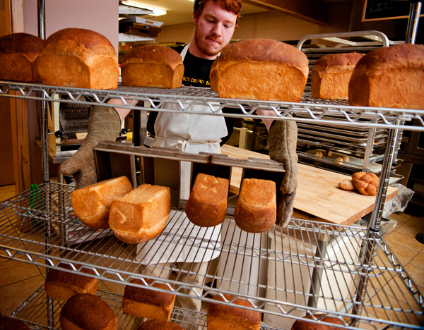 The Victorian Bakery assitant baker Cory Snyder places warm loaves  of oatmeal bread on the cooling rack