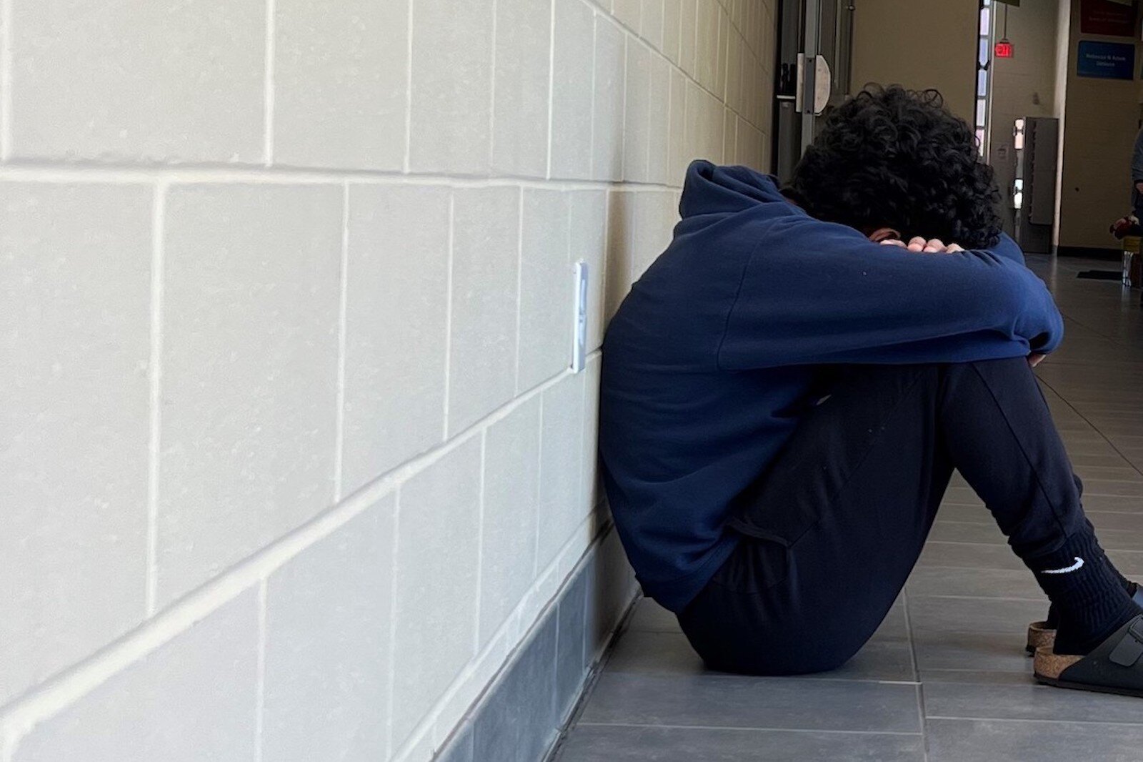 A high schooler sits by himself in a hallway.  He has fallen behind in class and doesn’t feel he has enough support from teachers throughout the pandemic in this photo staged for staged for illustrative purposes.