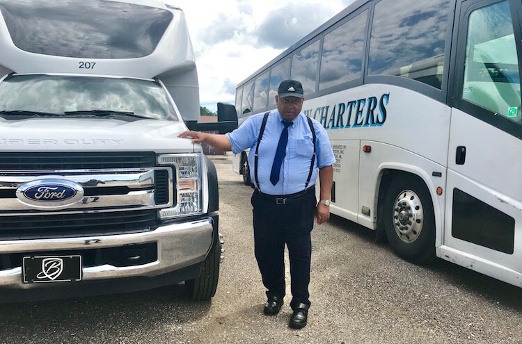 Gene Wright, co-owner of B&W Charters Inc., stands between a 30-passenger coach and a 56-passenger motor coach.