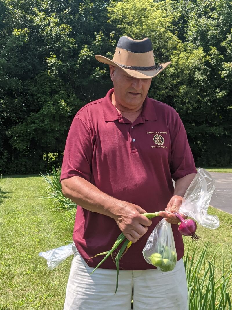 Carlos Fontana studies a red onion that he picked from his farm garden which will go inside a bag he is holding containing freshly-picked tomatillos.