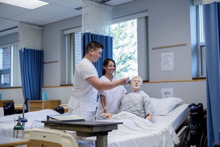 Two Certified Nursing Assistant students smile while practicing skill to take care of patients.