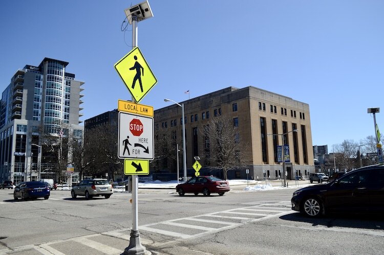 Solar-powered sign with flashing lights, which tells drivers it's the law to stop for pedestrians in crosswalks, hopefully stops all four lanes of Michigan Avenue traffic as they speed to the light at Rose. Kalamazoo's traffic and city planning depar