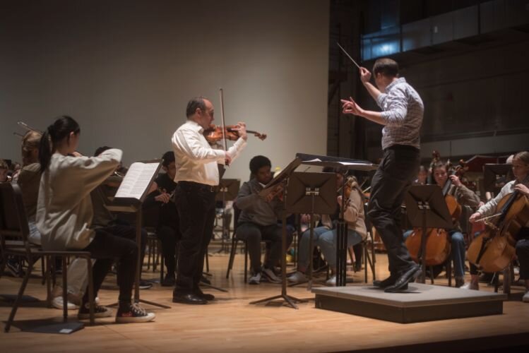 Conductor Andrew Koehler, violinist Mitchell Newman, and student musicians rehearse Paths to Dignity at Chenery Auditorium.